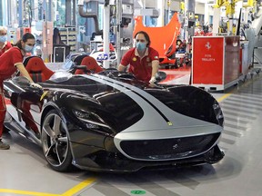 Ferrari workers in masks and gloves roll a car out of the assembly facility in May 2020.