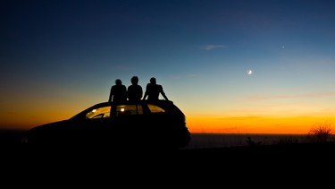 Two people sitting on a car during sunset