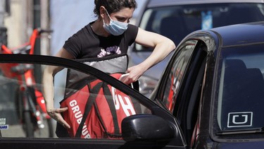 Food delivery driver Dori McGuire Guy wears a protective mask as she loads a take-out order into her car at the Pike Place Market, Friday, March 20, 2020, in Seattle.