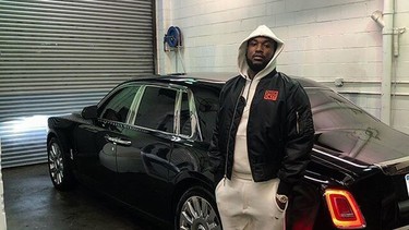 Rapper Meek Mill standing next to his black 2018 Rolls-Royce Phantom