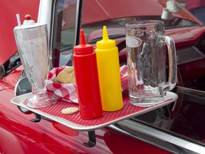 A drive-in restaurant's condiment tray hanging off the window of a classic Chevy convertible