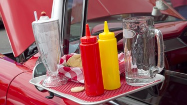 A drive-in restaurant's condiment tray hanging off the window of a classic Chevy convertible