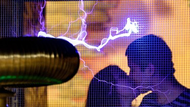This photo taken late on February 13, 2016 shows a couple exchanging a kiss by a Faraday cage displaying electrical sparks of Tesla coil.