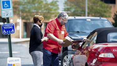 Election workers Tim McLeod and Cybil Usual assist a voter casting their ballot curbside on the first day of early voting at the Office of Elections satellite location at Southpoint in Spotsylvania, Virginia on Friday, September 18, 2020.