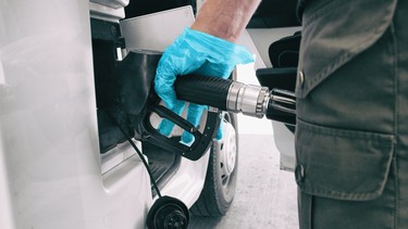 A man at a gas station wearing a blue medical glove to grab the refueling nozzle handle.