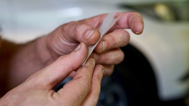Close up of hands rolling a joint in front of a car. Concept of impaired driving