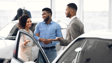 Couple Choosing Car Consulting With Professional Auto Salesman In Dealership