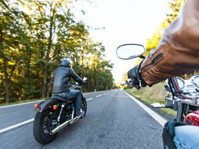 Two men riding motorcycles down a forested road