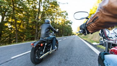 Two men riding motorcycles down a forested road