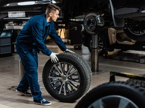 young mechanic holding car wheel near raised car in workshop