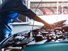 Car mechanic holding clipboard and checking to maintenance vehicle by customer claim order in auto repair shop garage. Engine repair service. People occupation and business job. Automobile technician