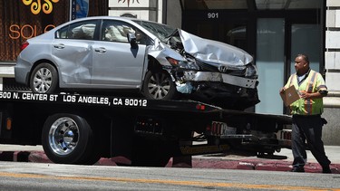 A tow truck driver walks past the damaged car after its driver was arrested on suspicion of felony hit-and-run after injuring six people in two incidents on Main Street in downtown Los Angeles on August 15, 2015.