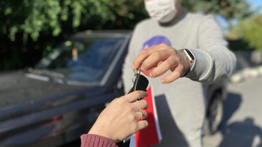 A used-car seller with a mask handing over the keys to the new owner