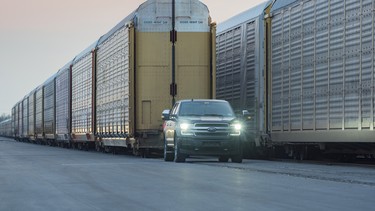 A prototype of the all-electric Ford F-150 Lightning pulls 10 rail cars loaded with 42 Ford trucks