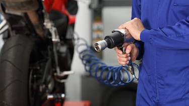 Close up of a motorcycle mechanic hand holding a pneumatic gun in a mechanical workshop