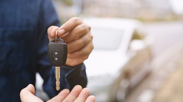 A car seller handing over the keys to a used car to a buyer.