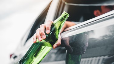 Drunk driver driving a car on the road holding bottle beer