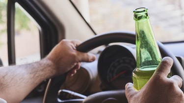 An unrecognizable man drinking beer while driving car. Concepts of driving under the influence, drunk driving or impaired driving