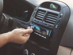 A man's hand twists the volume knob on a car radio.