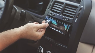 A man's hand twists the volume knob on a car radio.