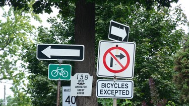 Sign overload at an intersection. This one-way street also has a two-lane bike lane going in both directions. Between the numerous signs, cyclists, e-scooters, and skateboarders it’s a challenging street to cross.
