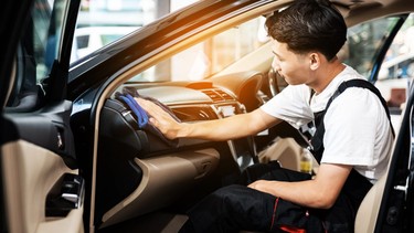 A man cleaning the interior car console with a dry blue microfiber towel, car detailing (or valeting) concept. Automobile professional cleaning service. Selective focus.