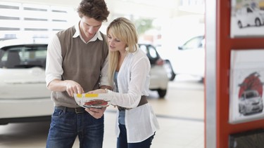 A couple looking over a brochure in a car dealership showroom.