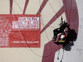 Activists of the environmental NGO Greenpeace climb a storage tank to glue posters during an action at the Dutch oil company Shell's refinery at the Pernis site in the port of Rotterdam on October 4, 2021, calling for an European Union ban on fossil fuel advertising.