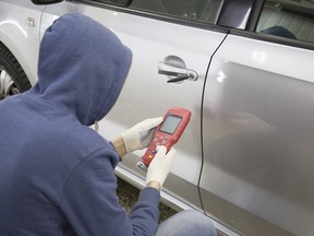 A hooded hacker-thief tries to break into a car's security system with a tablet.