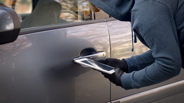 A hooded thief tries to break a car's security systems with a tablet