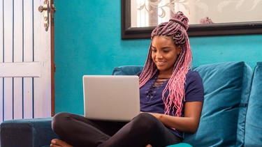 Young black woman with braid using notebook in home room