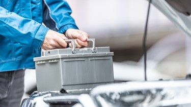 Mechanic replaces car battery in the car in the garage workshop.