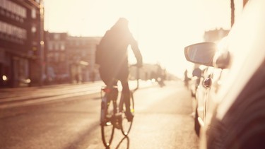 A cyclist going past a row of cars at sunset