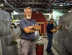 Der Restaurierungstechniker des National Air Force Museum of Canada, Mike Joly, steht zwischen zwei „Klappen“ des Lancaster KB 882-Flugzeugs des Museums, während der Freiwillige Dave Shepard am Donnerstag Farbe und Rost von dem Metall hinter sich abkratzt.  ALEX FILIPPE