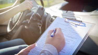 Examiner filling in driver's license road test form sitting with student inside a car