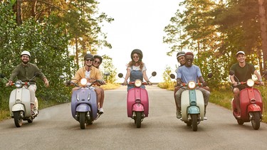 A group of young people riding scooters down the road