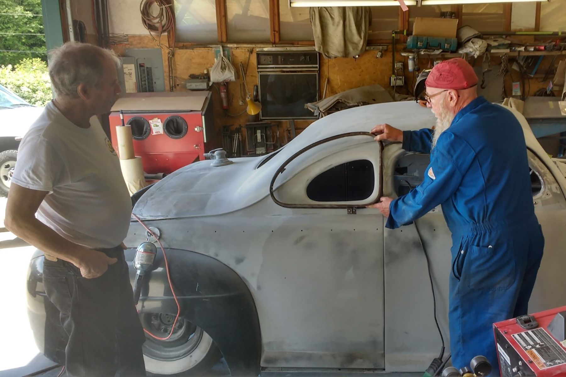 Lloyd Bingley’s friend Ken Tuppert holds up the original side window to show how much the roof line has been lowered in the 1946 Ford coupe. Ron Watts is looking on. CREDIT: Submitted