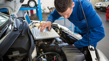 Mechanic consulting repair software while diagnosing a vehicle.