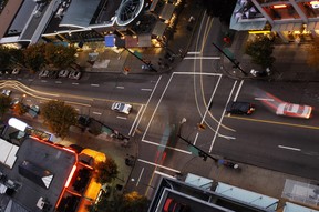 Eine von Vancouvers Kreuzungen in einem Einkaufsviertel in der Abenddämmerung, von oben gesehen, mit Autos, die die Spur wechseln, darauf warten, dass die Ampeln auf Grün schalten, beschleunigen, ausweichen und manövrieren