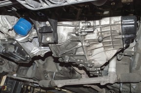 Bottom view of an automatic transmission and an internal combustion engine mounted on a car lifted on a lift in an auto repair shop
