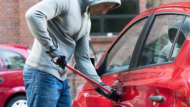 A car thief in a hooded jacket using a crowbar to open a car's door