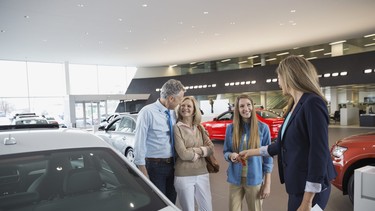Saleswoman handing family key in car dealership showroom