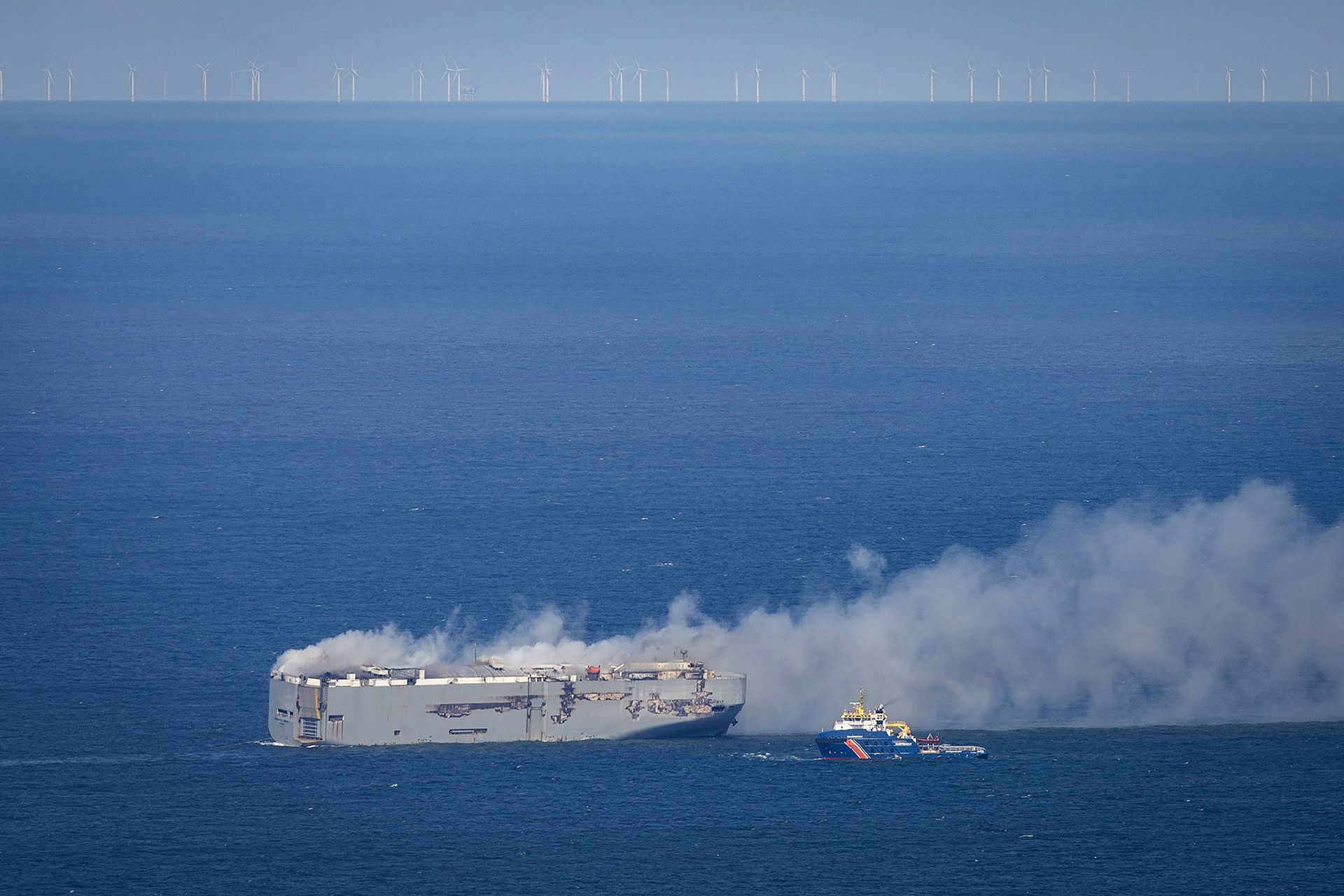 A Dutch coast guard boat (right) approaches the Panamanian-registered car carrier cargo ship Fremantle Highway on fire off the coast of the northern Dutch island of Ameland, on July 26, 2023