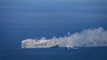A Dutch coast guard boat (right) approaches the Panamanian-registered car carrier cargo ship Fremantle Highway on fire off the coast of the northern Dutch island of Ameland, on July 26, 2023