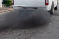 A diesel pickup truck "rolling coal" and leaving plumes of exhaust smoke on a road in a city