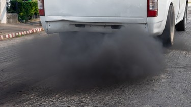 A diesel pickup truck "rolling coal" and leaving plumes of exhaust smoke on a road in a city