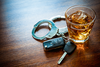 A pair of handcuffs and a set of car keys next to a drink DUI