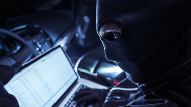 A thief using a laptop to hack into a car