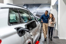 A couple walking through a car dealership, shopping for a new electric vehicle (EV)