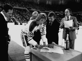 Wayne Gretzky signs a twenty one year contract with the Edmonton Oilers, then of the World Hockey Association, at centre ice Jan. 26 1979, before a game against Cincinnati Stingers. Helping Gretzky sign, on his eightteen birthday is Oilers general manager Larry Gordon. Standing on the left is Walter Gretzky, Wayne's father. Photo by Ken Orr, Edmonton Journal file